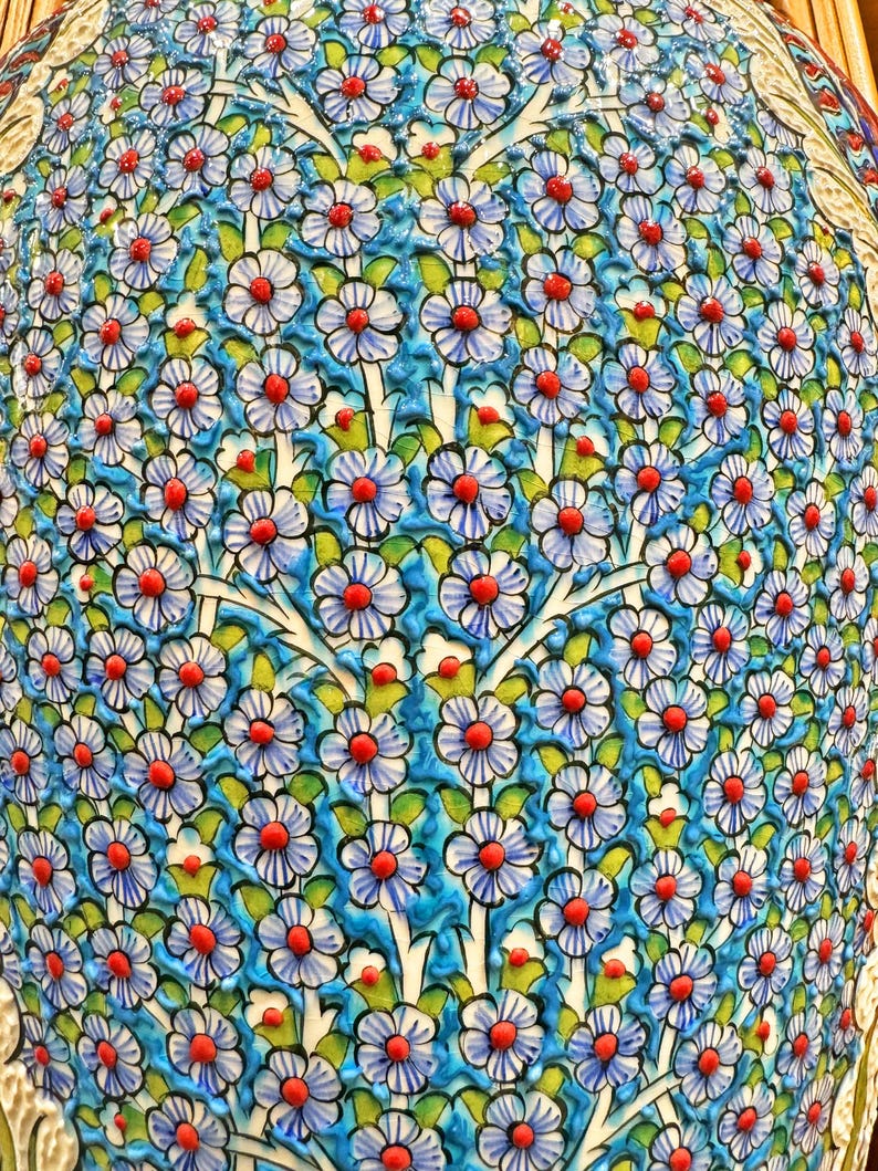 May include: A close-up of a ceramic vase with a blue and white floral pattern. The vase is covered in small, white flowers with red centers. The flowers are arranged in a repeating pattern.
