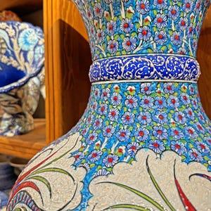 May include: A large, blue and white ceramic vase with intricate floral designs. The vase has a wide mouth and a narrow base, and is decorated with red, green, and white accents. The vase is a traditional Turkish design.