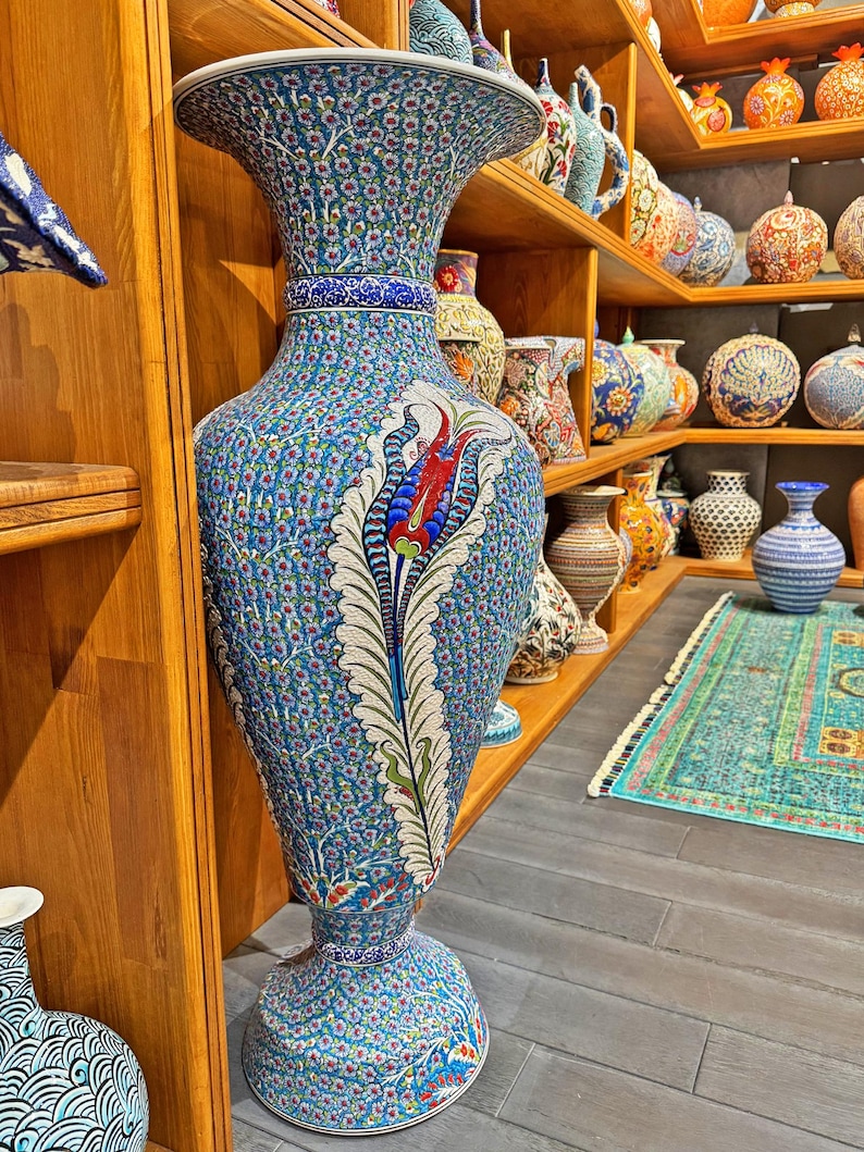 May include: A large, blue and white ceramic vase with intricate floral designs and a red tulip. The vase is on a wooden shelf with other ceramic vases.