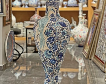 May include: A tall, white ceramic vase with a blue and white floral pattern. The vase has a wide mouth and a narrow base. The floral pattern includes peacocks, flowers, and leaves.