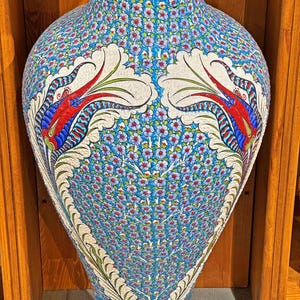May include: A large, blue and white ceramic vase with intricate floral and bird designs. The vase has a wide base and a narrow neck.