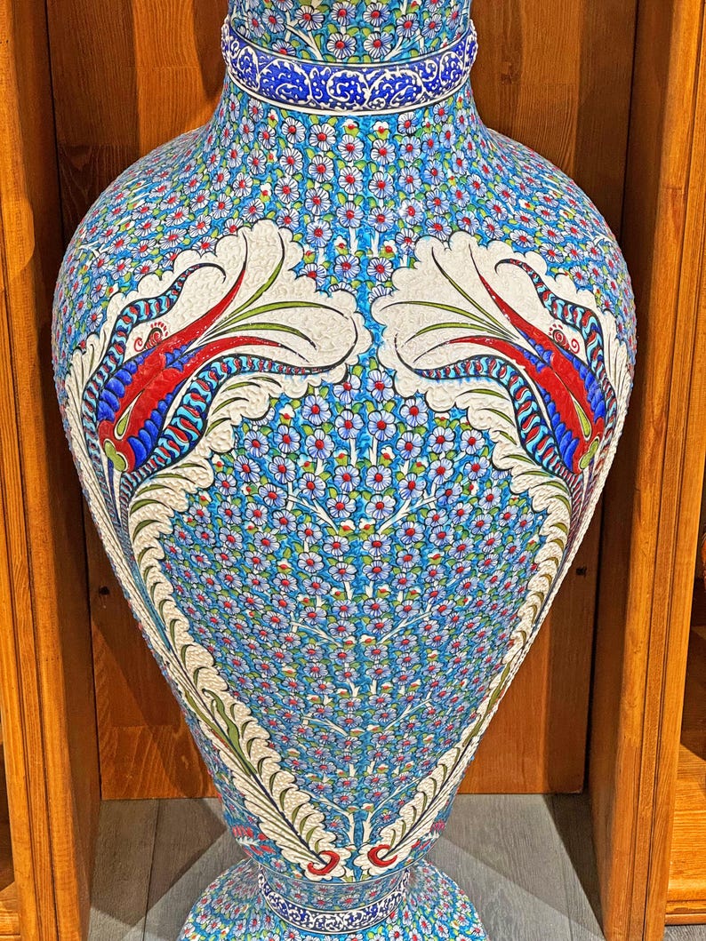 May include: A large, blue and white ceramic vase with intricate floral and bird designs. The vase has a wide base and a narrow neck.