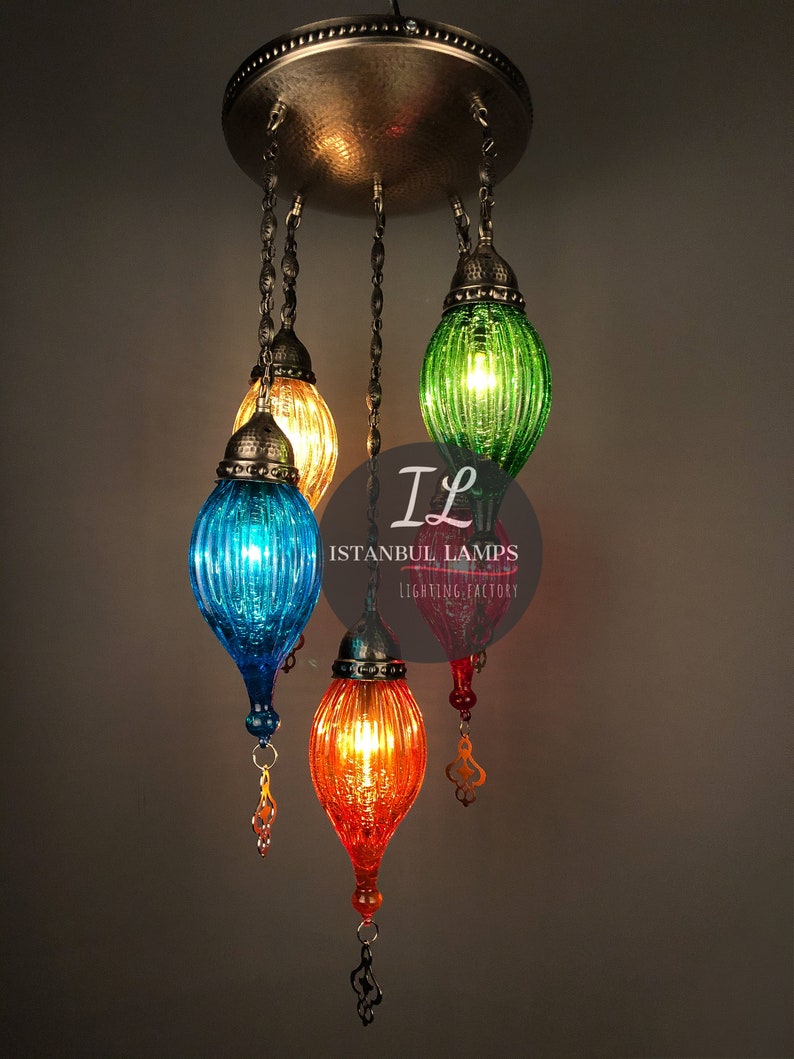 Puede incluir: Una l&aacute;mpara de ara&ntilde;a de vidrio multicolor con cinco luces. Las pantallas de vidrio son verdes, azules, naranjas y amarillas. La l&aacute;mpara de ara&ntilde;a cuelga de una fijaci&oacute;n de techo de metal. El texto "Istanbul Lamps Lighting Factory" es visible en la imagen.