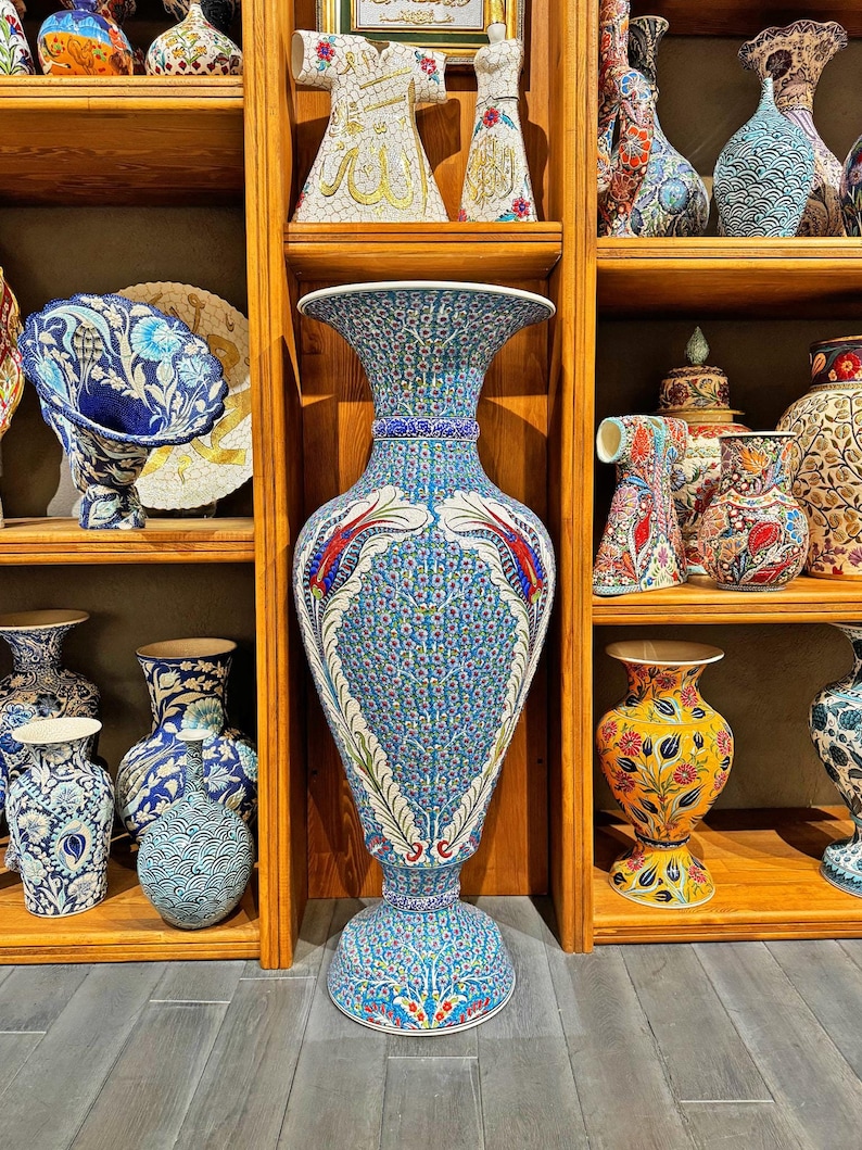 May include: A large, blue and white ceramic vase with intricate floral and geometric patterns. The vase is on a wooden shelf with other decorative ceramic items.