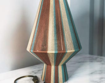 May include: A striped table lamp with a brown, beige, and blue patterned shade. The lamp has a gold cord and a white marble base.