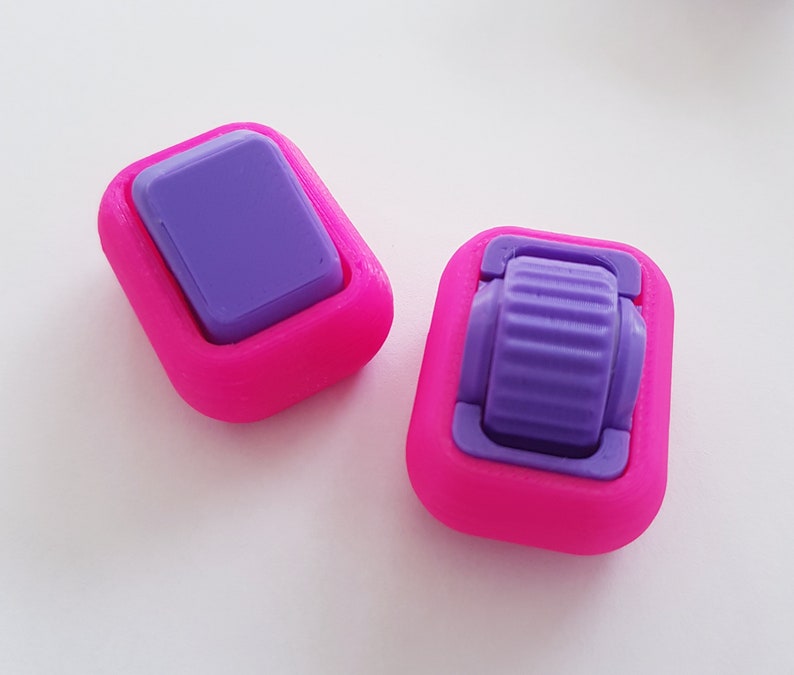 May include: Two pink plastic toggles with purple accents. The toggles are square shaped and have a small, round, purple button in the centre.