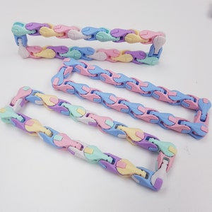 Puede incluir: Tres cadenas flexibles de colores hechas de plástico en colores pastel de rosa, azul, amarillo y verde. Los eslabones están conectados y se pueden manipular para formar diferentes formas.