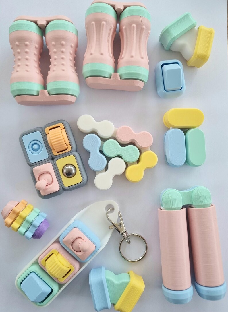 Puede incluir: Una colecci&oacute;n de juguetes fidget coloridos en varias formas y dise&ntilde;os. Los juguetes presentan colores pastel rosa, azul, amarillo y verde. Algunos tienen botones, rodillos y otros elementos interactivos. Tambi&eacute;n se incluye un llavero con juguetes fidget similares.