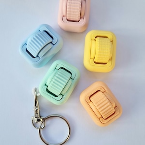 May include: Five colourful plastic keyrings with a rotating wheel feature. Each keyring is a different pastel colour: light blue, light green, light pink, light orange, and yellow. A silver keyring ring is included.
