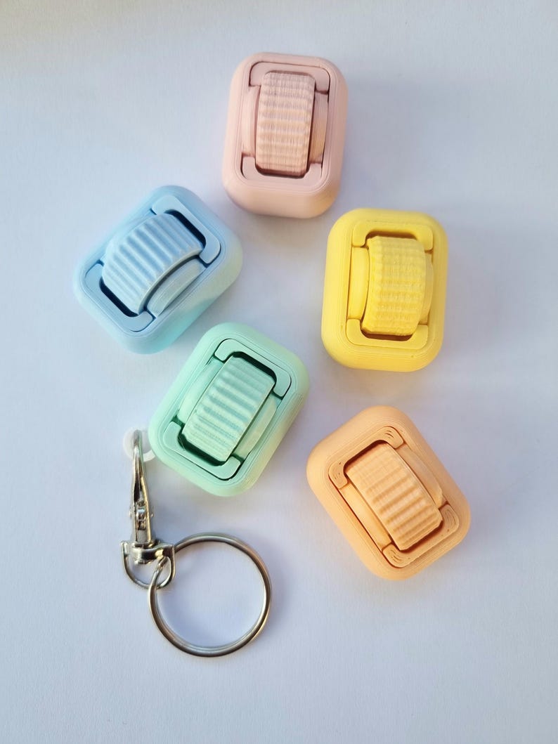 May include: Five colourful plastic keyrings with a rotating wheel feature. Each keyring is a different pastel colour: light blue, light green, light pink, light orange, and yellow. A silver keyring ring is included.