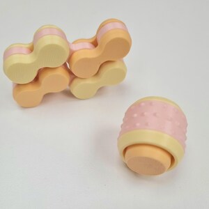 May include: A set of five connected, pastel-colored, plastic fidget toys. The toys are shaped like a chain link and have a textured surface. The toys are in a light pink, light yellow, and orange color scheme.