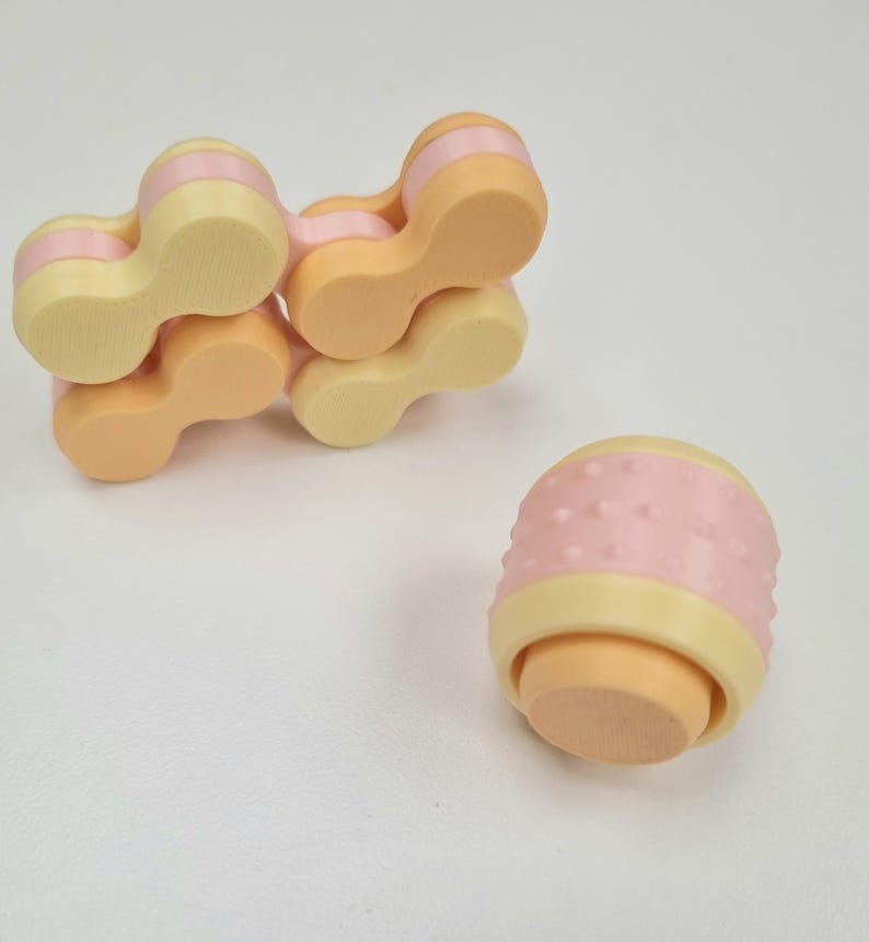 May include: A set of five connected, pastel-colored, plastic fidget toys. The toys are shaped like a chain link and have a textured surface. The toys are in a light pink, light yellow, and orange color scheme.