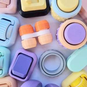 May include: Assortment of colorful, small, plastic toys with various shapes and designs. Some toys have a knob or button on top, while others have a ring or a slider. The toys are arranged on a white surface.