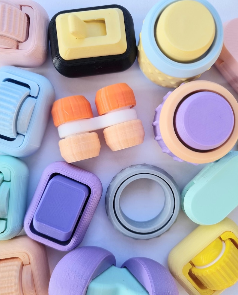 May include: Assortment of colorful, small, plastic toys with various shapes and designs. Some toys have a knob or button on top, while others have a ring or a slider. The toys are arranged on a white surface.