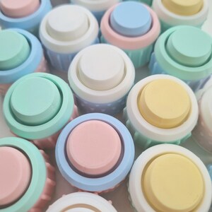 May include: A collection of pastel-colored round buttons with a white rim. The buttons are arranged in a random pattern and are made of a smooth, plastic-like material.