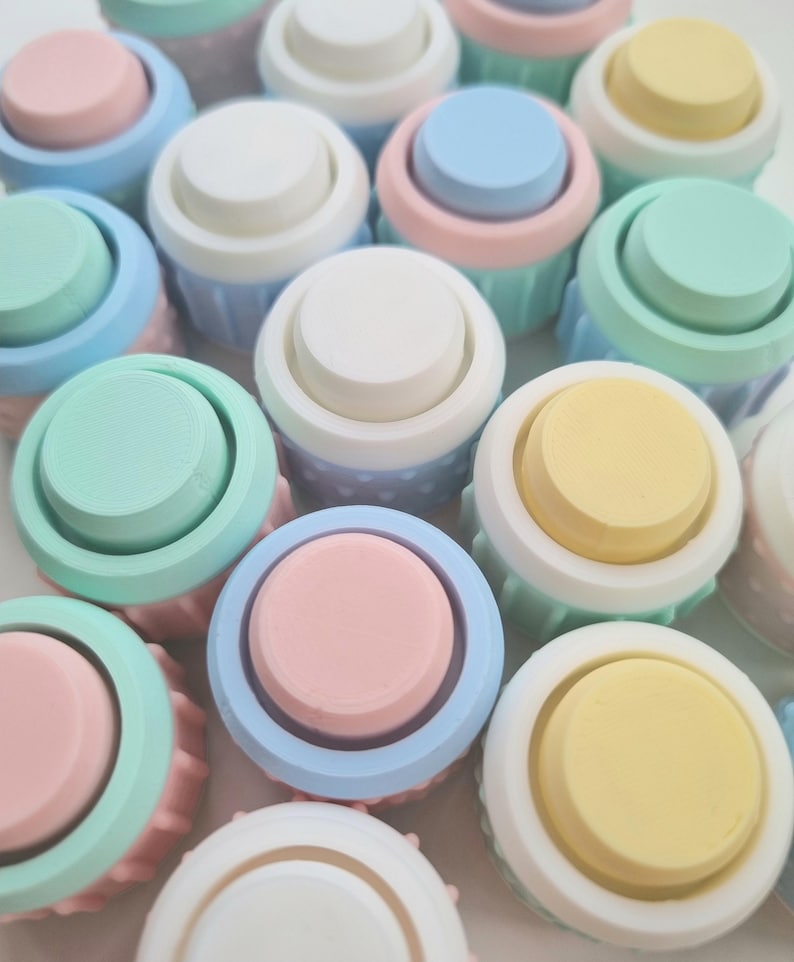 May include: A collection of pastel-colored round buttons with a white rim. The buttons are arranged in a random pattern and are made of a smooth, plastic-like material.