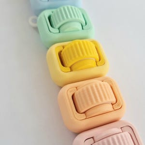 May include: A set of six colourful plastic rollers, each with a different colour, arranged in a rainbow pattern from purple to pink. The rollers are designed for use in crafts and hobbies.