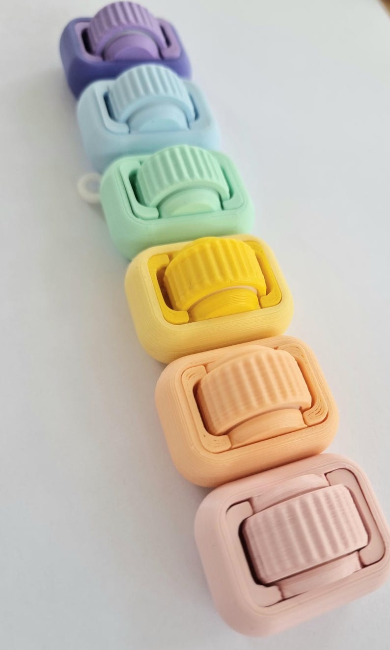 May include: A set of six colourful plastic rollers, each with a different colour, arranged in a rainbow pattern from purple to pink. The rollers are designed for use in crafts and hobbies.