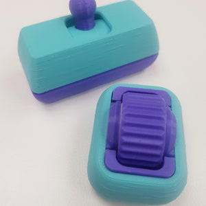 May include: Two 3D printed objects, one is a teal and purple toggle switch with a purple knob, the other is a teal and purple wheel with a purple gear.