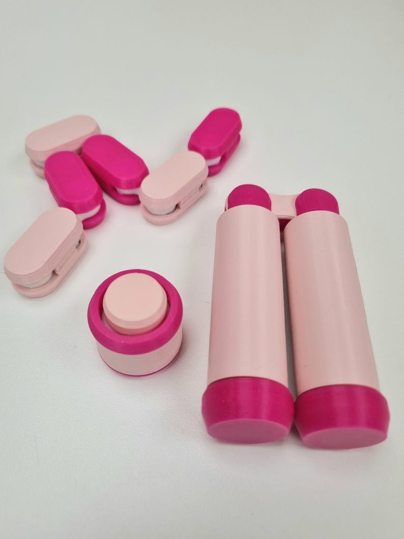 May include: A set of pink and magenta phone stand accessories. The set includes a small round stand and two long, cylindrical stands.