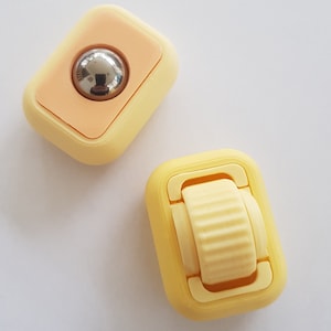 May include: Two small yellow plastic fidget toys. One toy has a round, silver ball that spins. The other toy has a small yellow wheel that spins.
