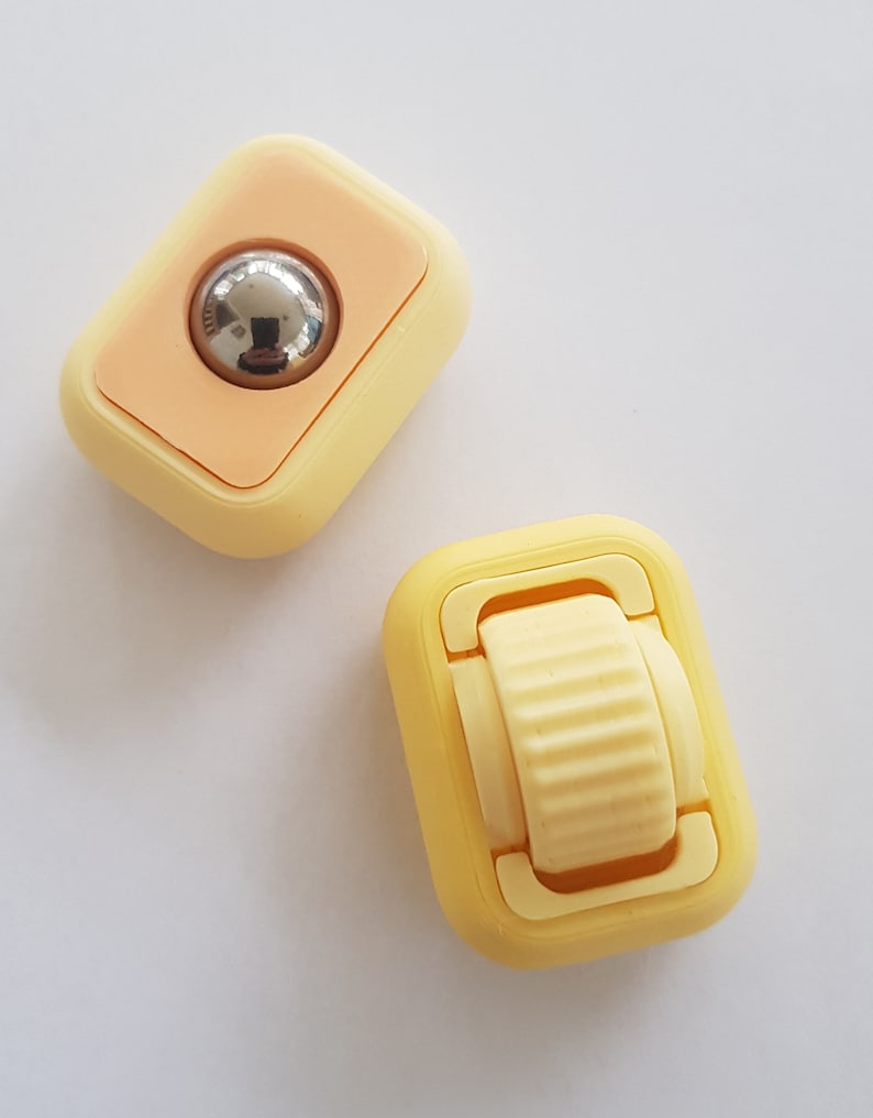 May include: Two small yellow plastic fidget toys. One toy has a round, silver ball that spins. The other toy has a small yellow wheel that spins.