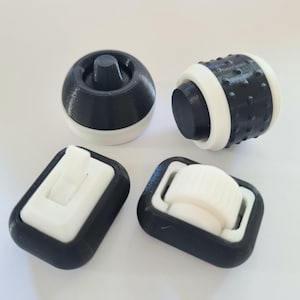 May include: Four black and white plastic furniture caster wheels. Two of the wheels are round and have a textured surface. The other two wheels are rectangular and have a smooth surface.