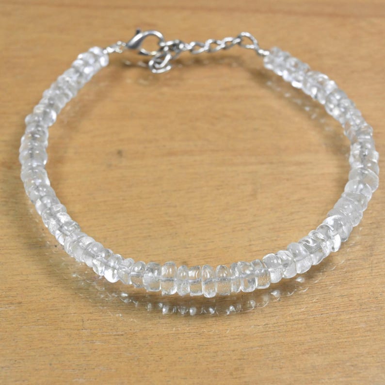 May include: A clear quartz bracelet with a silver-colored clasp. The bracelet is made of small, faceted, clear quartz beads strung together. The beads are uniform in size and shape, creating a delicate and elegant piece of jewelry.