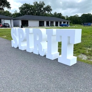May include: White foam letters spelling out the word "SPIRIT" on a paved driveway. The letters are large and stand upright.