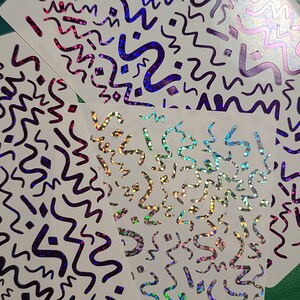 May include: Four sheets of white paper with a holographic, iridescent finish. Each sheet has a repeating pattern of black wavy lines and shapes.