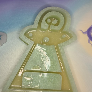 May include: A green and white glitter resin mold of a UFO. The mold is filled with resin and has a glittery finish.