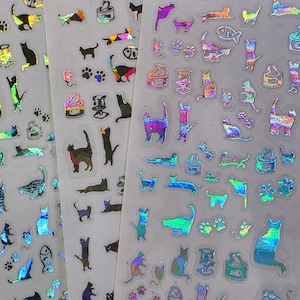 May include: Sheets of iridescent cat stickers in various poses, including standing, sitting, and lying down. The stickers feature cat paw prints and images of cat food cans. The stickers have a holographic effect, reflecting multiple colors.