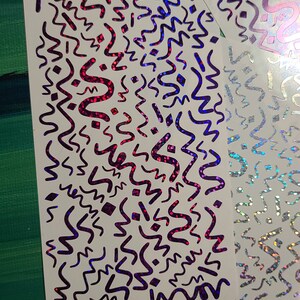 May include: Two sheets of white paper with a holographic, iridescent finish. The paper is decorated with a repeating pattern of black wavy lines and geometric shapes. The holographic finish creates a rainbow effect.