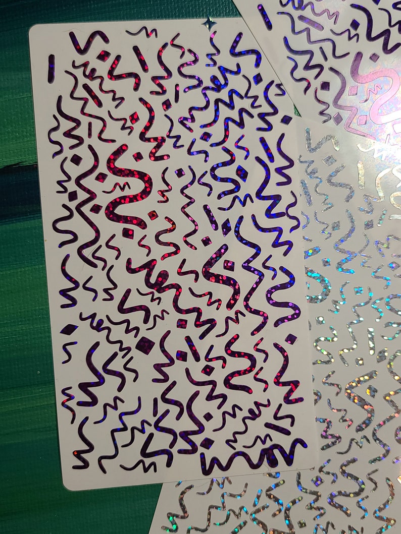 May include: Two sheets of white paper with a holographic, iridescent finish. The paper is decorated with a repeating pattern of black wavy lines and geometric shapes. The holographic finish creates a rainbow effect.