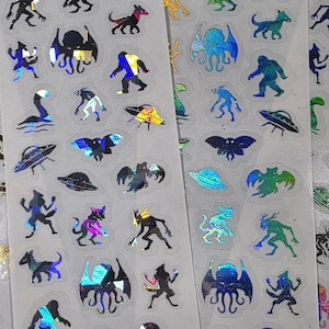 May include: Sheets of holographic stickers featuring various cryptids and UFOs. Designs include Bigfoot, the Loch Ness Monster, aliens, and flying saucers. The stickers have a shiny, iridescent finish, with colors like blue, green, and purple.