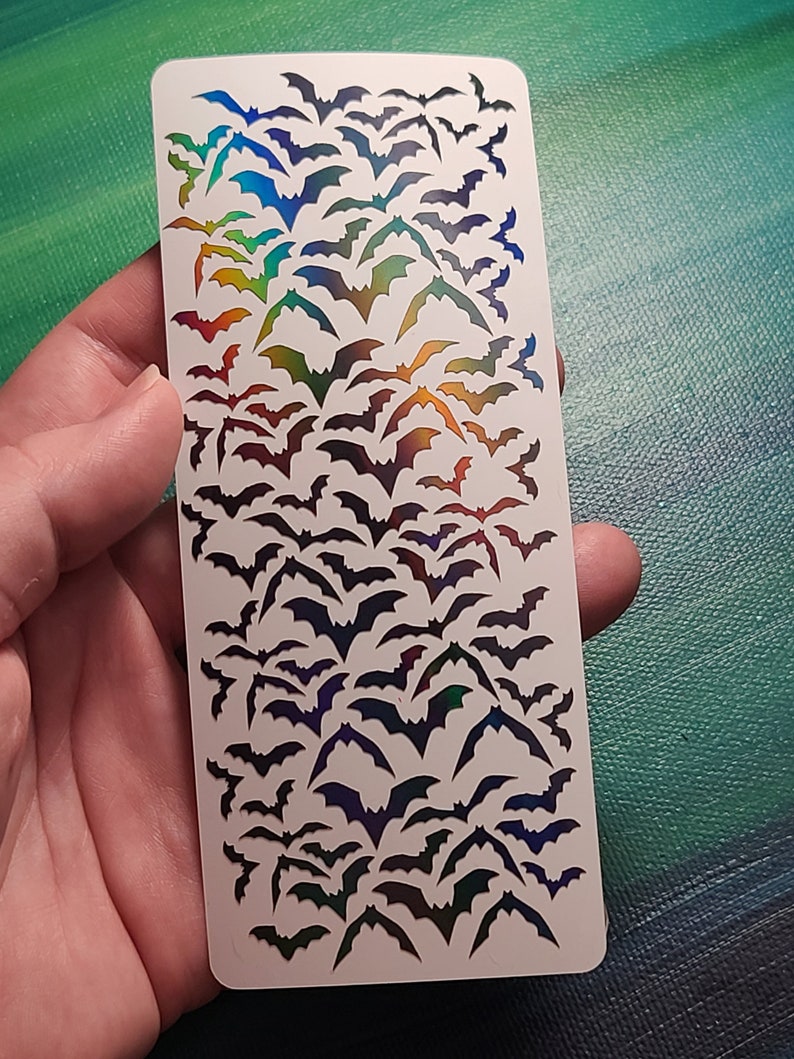 Peut inclure: Une feuille de papier autocollant blanc avec une finition arc-en-ciel iris&eacute;e. Le papier est rempli d'un motif de silhouettes de chauves-souris.