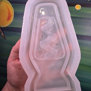 May include: A clear, flexible silicone mold in the shape of a lava lamp. The mold has a detailed interior design, with the outline of the lava lamp's shape and internal features. The mold is held in a hand, with a painted background.