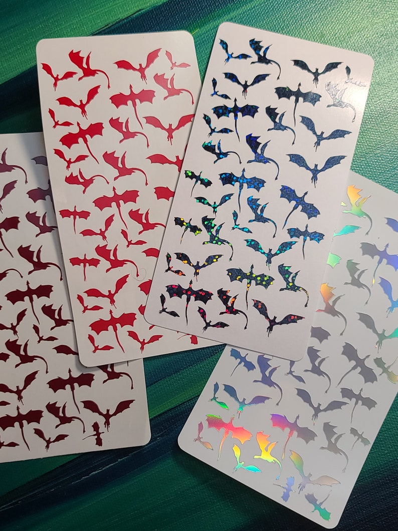 May include: Four sheets of stickers featuring various dragon designs. The stickers are on white cardstock and feature red, black, and iridescent holographic dragons.