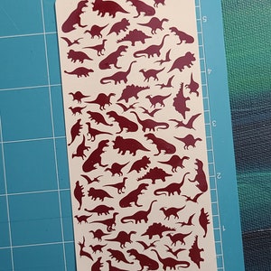 Puede incluir: Una hoja de papel adhesivo blanco con una silueta roja de varios dinosaurios. Los dinosaurios est&aacute;n dispuestos en filas y columnas, con una variedad de tama&ntilde;os y formas.