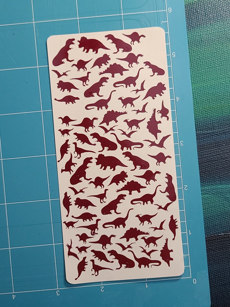 Puede incluir: Una hoja de papel adhesivo blanco con una silueta roja de varios dinosaurios. Los dinosaurios est&aacute;n dispuestos en filas y columnas, con una variedad de tama&ntilde;os y formas.