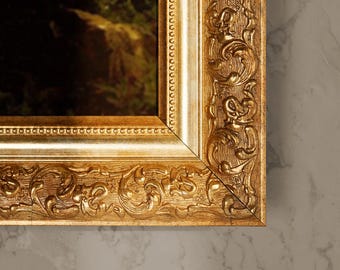 May include: Close-up of a gold-colored picture frame with ornate, carved details. The frame has a rectangular shape with a beveled edge and a detailed floral and scroll pattern. The artwork within the frame is partially visible, with green and brown tones.