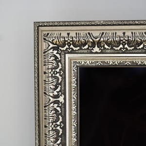May include: Close-up of a decorative silver picture frame with ornate detailing. The frame has a black interior and a silver and black border. The design features intricate patterns and a classic aesthetic.