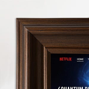 May include: A dark brown wooden picture frame with a ridged texture. The frame surrounds a screen with the Netflix logo and the word "HOME". The bottom of the screen has the words "QUANTUM DI..."