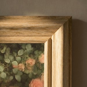 Könnte beinhalten: Nahaufnahme eines gerahmten Blumendrucks. Der Rahmen besteht aus hellem Holz mit natürlicher Maserung. Das Kunstwerk zeigt ein unscharfes Bild von rosa Rosen und grünem Laub.