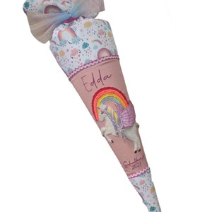 May include: Pink and white school cone with a unicorn and rainbow design. The cone is decorated with a pink ribbon and the name "Edda" is embroidered on the front. The text "Schulkind 2023" is also embroidered on the cone.