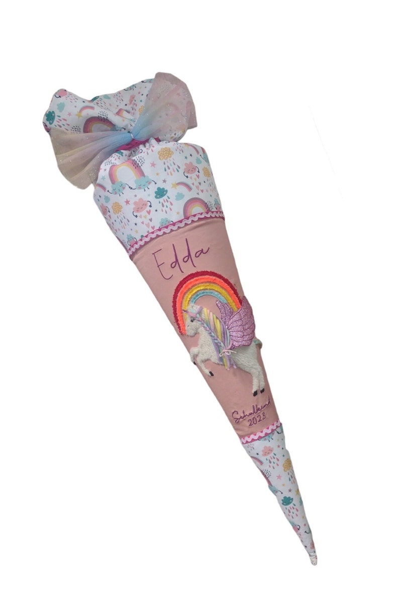 May include: Pink and white school cone with a unicorn and rainbow design. The cone is decorated with a pink ribbon and the name "Edda" is embroidered on the front. The text "Schulkind 2023" is also embroidered on the cone.