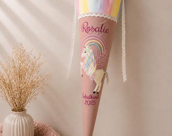 May include: A cone-shaped school gift bag in dusty pink fabric featuring an embroidered unicorn with a rainbow and wings. The name Rosalie and the text Schulkind 2025 are embroidered in dark pink. It has a pastel rainbow fabric top with white lace.