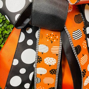K&ouml;nnte beinhalten: Nahaufnahme einer Halloween-Kranz mit schwarz-wei&szlig;em Polka-Dot-Band, orangefarbenem Band mit wei&szlig;en K&uuml;rbis-Designs und schwarzem Band mit wei&szlig;-schwarzem Gingham-Besatz.