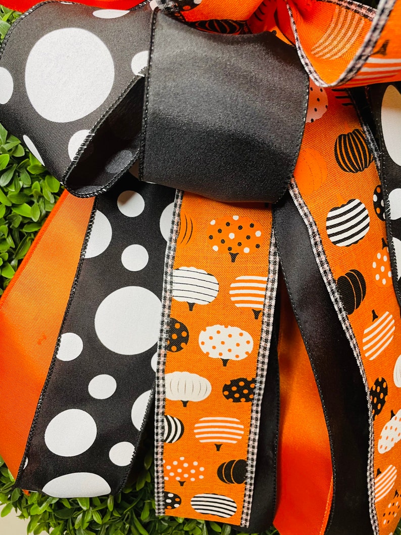 K&ouml;nnte beinhalten: Nahaufnahme einer Halloween-Kranz mit schwarz-wei&szlig;em Polka-Dot-Band, orangefarbenem Band mit wei&szlig;en K&uuml;rbis-Designs und schwarzem Band mit wei&szlig;-schwarzem Gingham-Besatz.