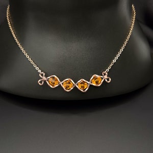 Può includere: Una collana con catena dorata con un design in filo di rame con quattro cristalli quadrati di colore ambrato.